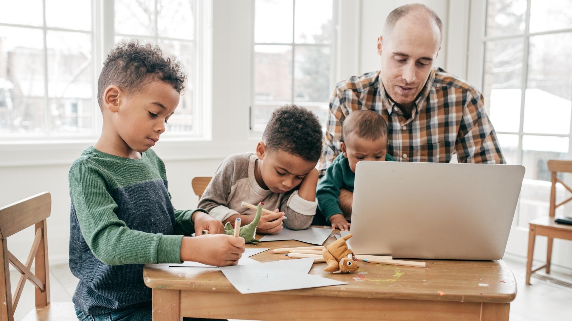 A dad working at the kitchen table with his kids beside him
